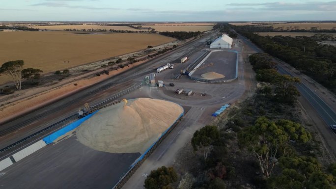 西澳大利亚，谷物货车在格栅中卸货，谷物从堆垛机上掉落。夕阳下的空中风景