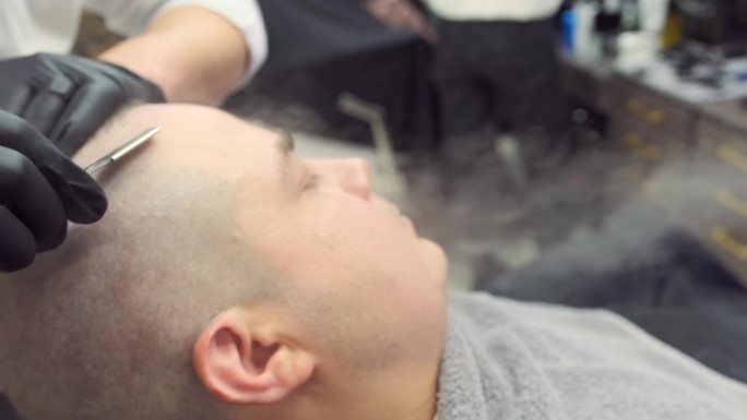 一名男子在用剃刀剃须时，蒸汽发生器喷出的热蒸汽湿润了他的头部