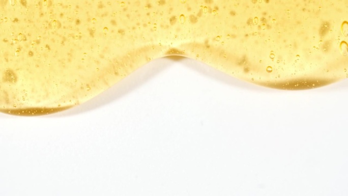 黄色化妆品凝胶流体与分子气泡流动在纯白色背景。液体乳霜凝胶。天然有机化妆品、药品微距拍摄。生产特写。