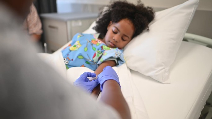 友好的非洲护士在病房的病床上给小女孩的手臂上打点滴