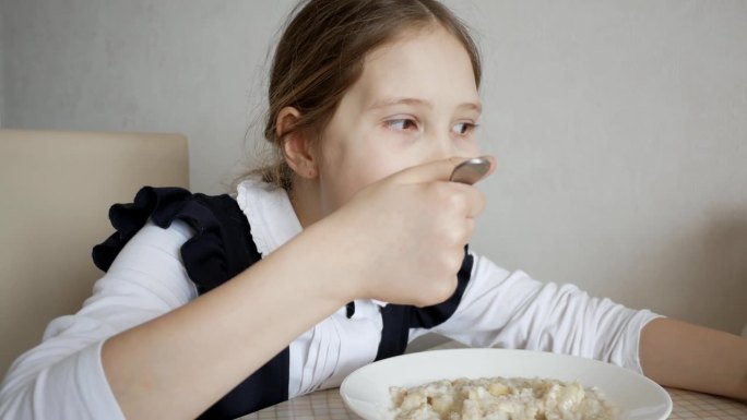 穿校服的女学生在学校食堂吃粥的特写。十几岁的女孩吃早餐或午餐。学校健康饮食的概念。