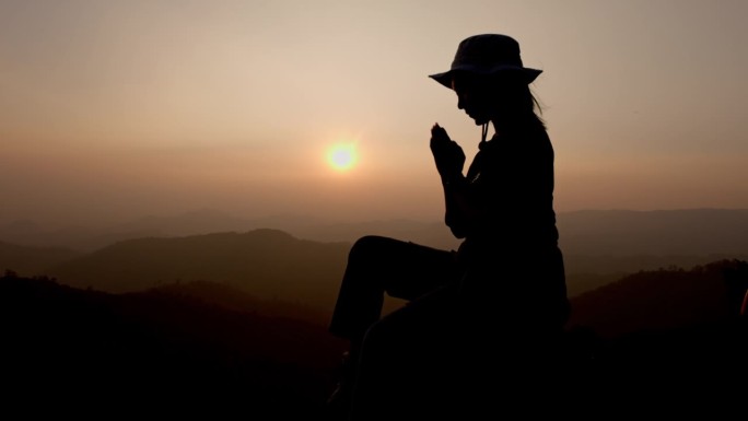 一个女人在山上祈祷的剪影，用对宗教的信仰和对上帝的信仰祈祷。