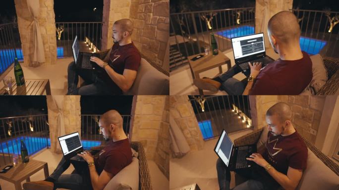 晚上，秃顶的年轻人坐在沙发上，在别墅阳台上的笔记本电脑上工作