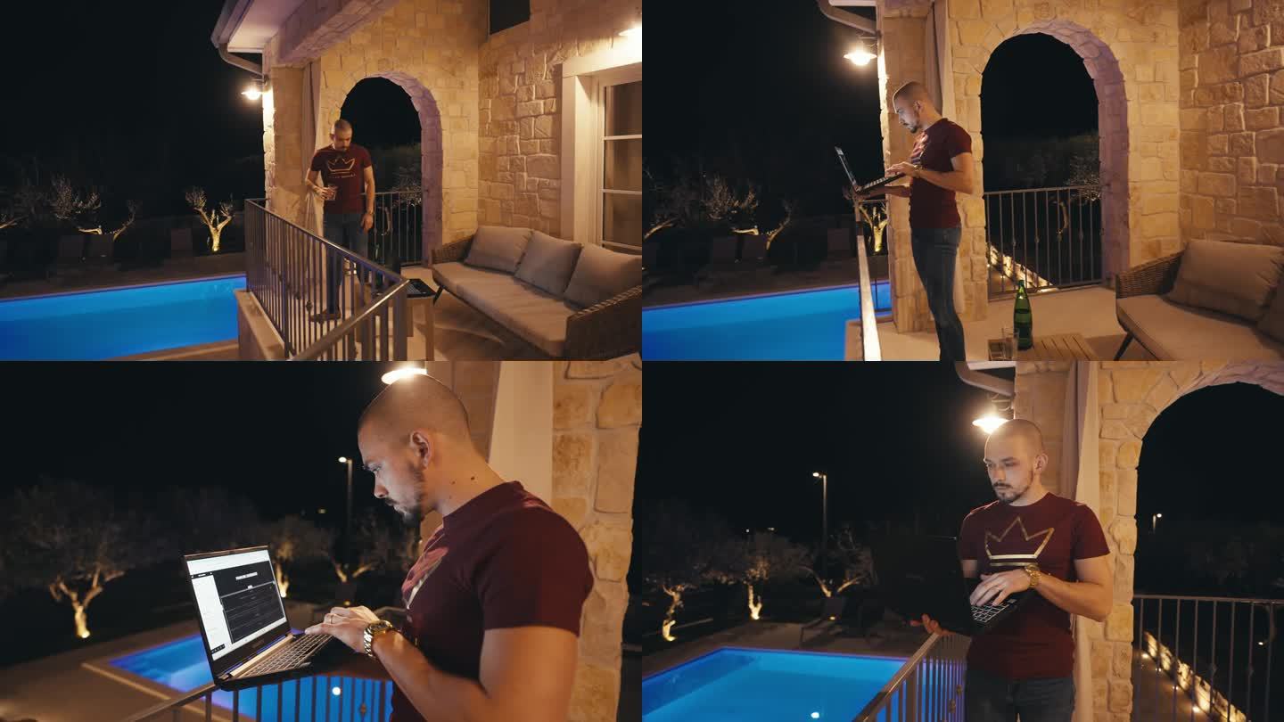 晚上在带游泳池的别墅阳台上喝完水后使用笔记本电脑的秃头年轻人