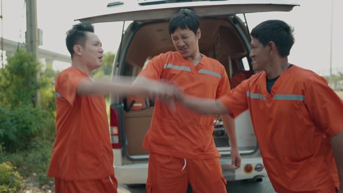 三名身着制服的亚洲人救援队队员手牵手，共同庆祝救援成功。快乐救援队携起手来，工作顺利。团队合作，成功