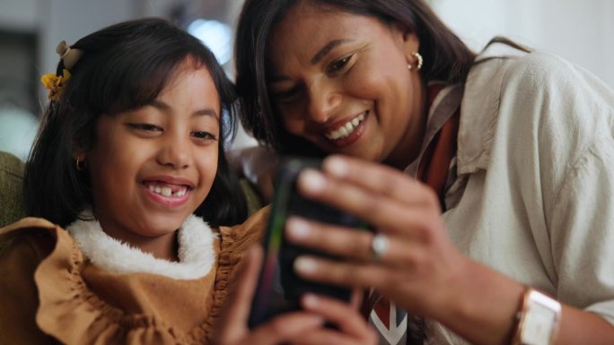 微笑，孩子和妈妈在家里用手机，学习或看卡通，家庭纽带在一起。快乐的妈妈，女孩和智能手机的互联网应用程