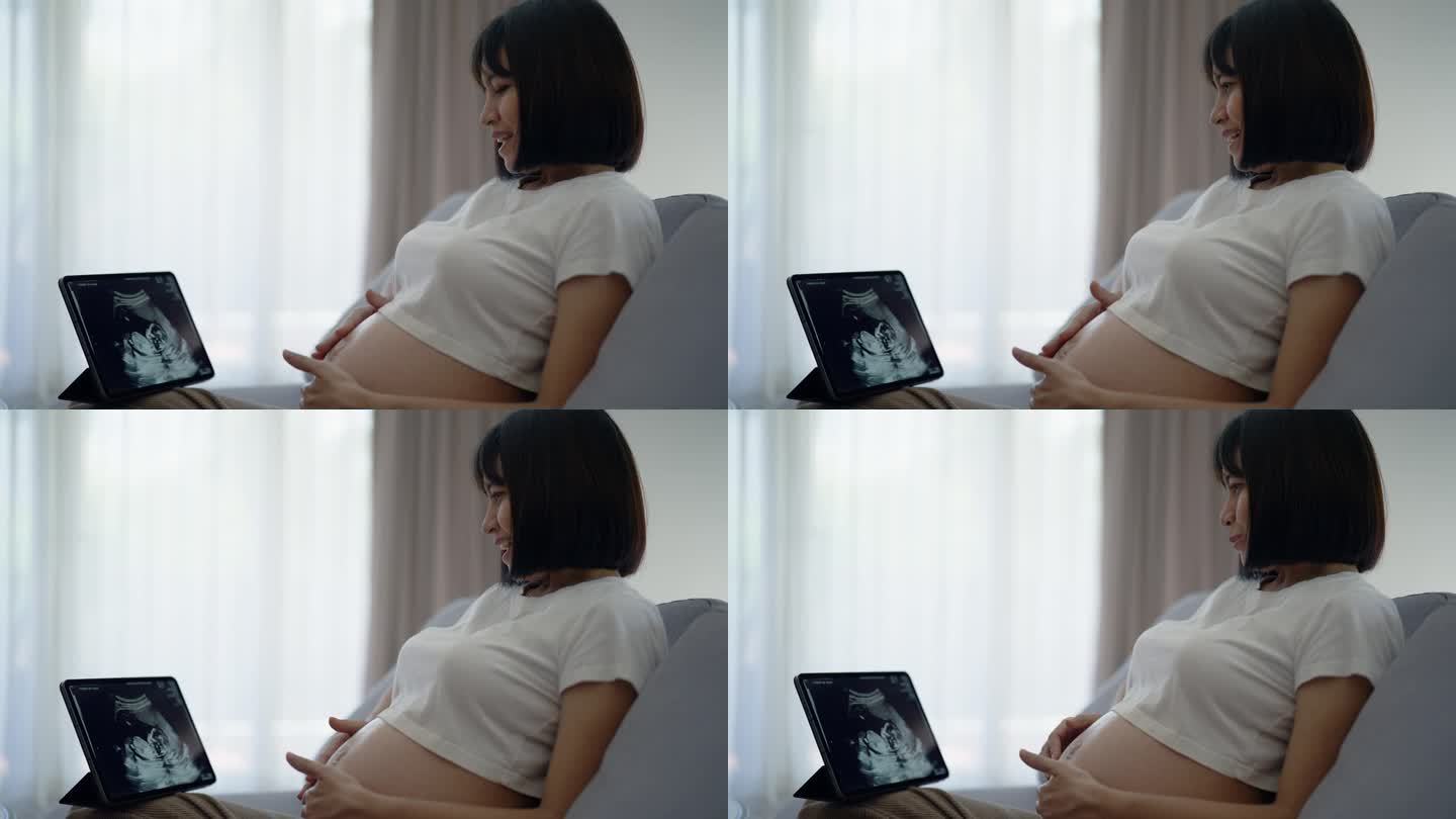 年轻的怀孕母亲高兴地看着平板上的超声波片，与她的孩子交谈。