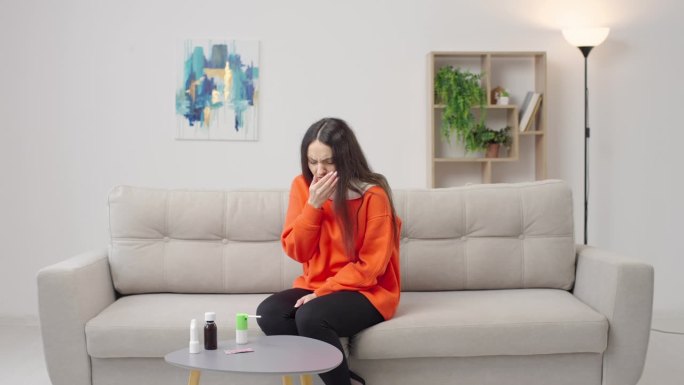 患有喉咙痛的年轻女子戴着围巾坐在沙发上喷雾剂
