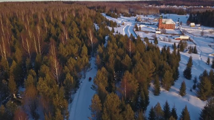 冬季森林中雪地摩托和村庄的俯视图。夹。雪地摩托驶往老村庄的电影画面。冬季，以村庄和山脉为背景的森林雪