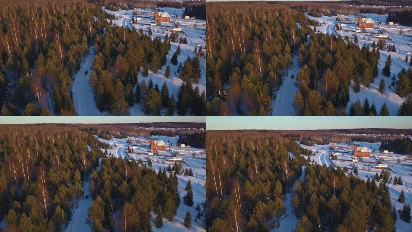 冬季森林中雪地摩托和村庄的俯视图。夹。雪地摩托驶往老村庄的电影画面。冬季，以村庄和山脉为背景的森林雪