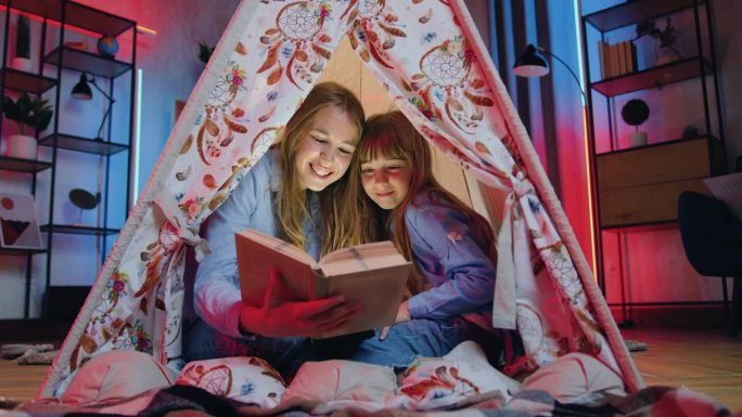 两个不同年龄的女孩姐妹的特写，她们在家里和看书中度过了共同的闲暇时光