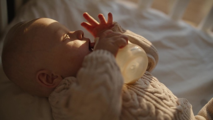SLO MO滋养的爱:婴儿男孩在日落时从瓶子里吃东西