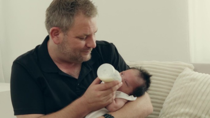 父亲与婴儿的亲密关系:父亲给刚出生的女儿喂奶的温情场景——家庭幸福。