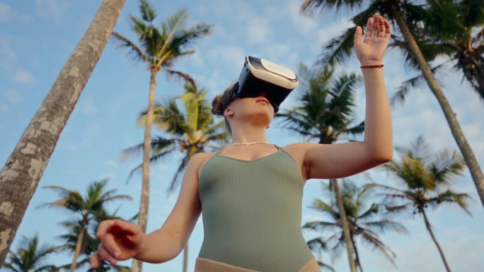 一名女子在棕榈树中使用VR耳机探索虚拟世界。数字世界的沉浸式体验。手势表示与虚拟环境的互动和参与。缓