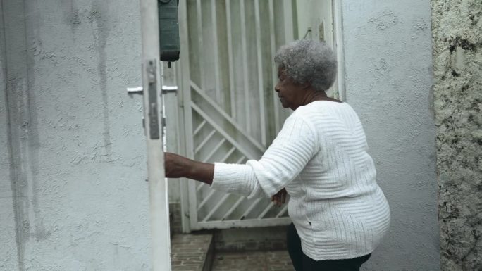 老年南美黑人妇女从人行道到家，在她身后关上门打开住宅大门返回，老年80年代的非洲裔人