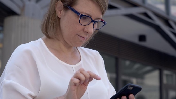 在户外，一位身穿白色衣服的黑发女子正全神贯注地发信息，用她的智能手机拉近距离。