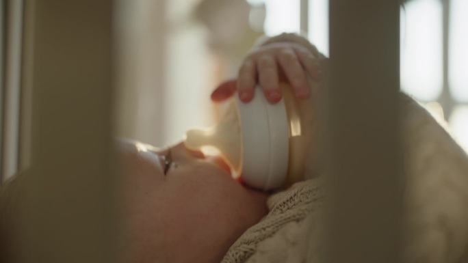 健康婴儿营养:男婴在他的婴儿床里喝奶瓶里的牛奶