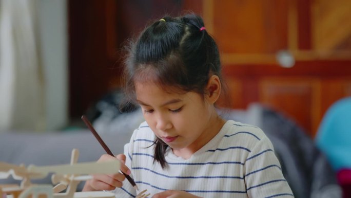亚洲女孩正在用铅笔色给组装的木制玩具上色