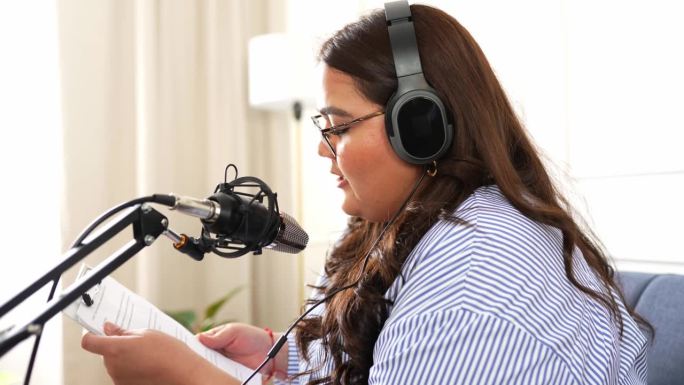 一个漂亮的胖女人戴着耳机对着麦克风说话，同时在她的客厅里录制播客