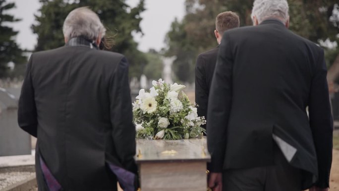 男子、棺材和护柩者走在墓葬室外的墓地仪式上。葬礼上的死亡，悲伤和集体棺材，在大风事件中运送到墓地和哀