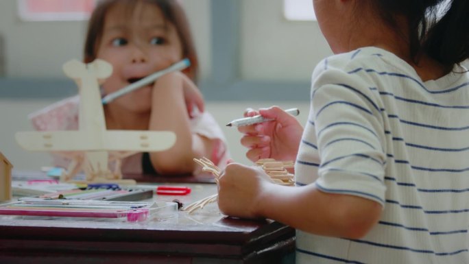 一个亚洲小女孩正在和她的姐姐一起给组装的木制玩具上色