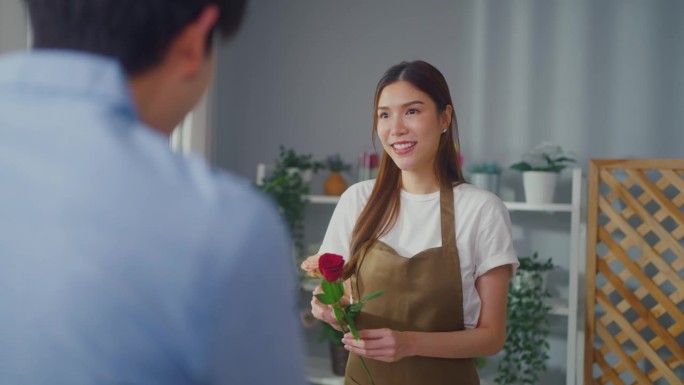 亚洲年轻的花店女孩在店里向顾客兜售漂亮的花束。有魅力的女小企业主在花店给男买家送鲜花礼物时感到快乐和