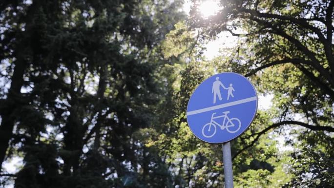 圆形道路标志表示自行车道和行人道优先。交通标志白色自行车在蓝色的圆圈，背景是树木和天空。生态交通基础