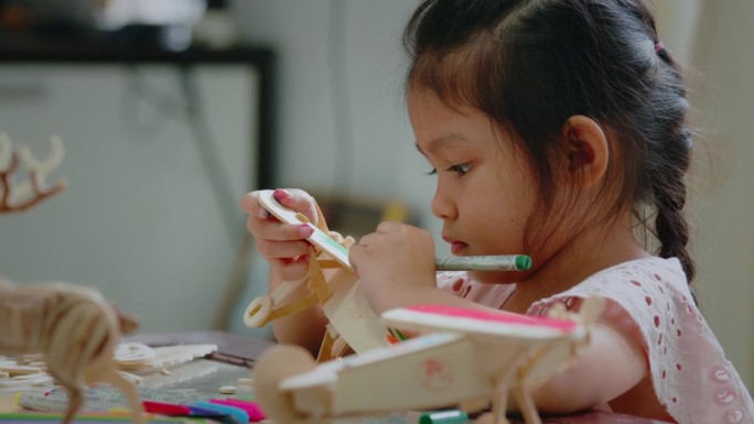 亚洲女孩正在用神奇的颜色给组装的木制玩具上色