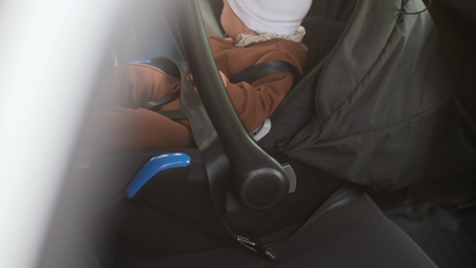 特写:无法辨认的父母正为坐在汽车后座上哭闹的男婴系安全带。乘车时系上安全带的伤心孩子。