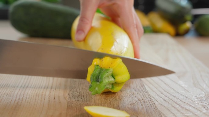厨师用手中的刀子切掉黄绿西葫芦的尾巴，木桌上放着蔬菜，家常菜，素菜，蔬菜，饮食。特写，正面，宏观