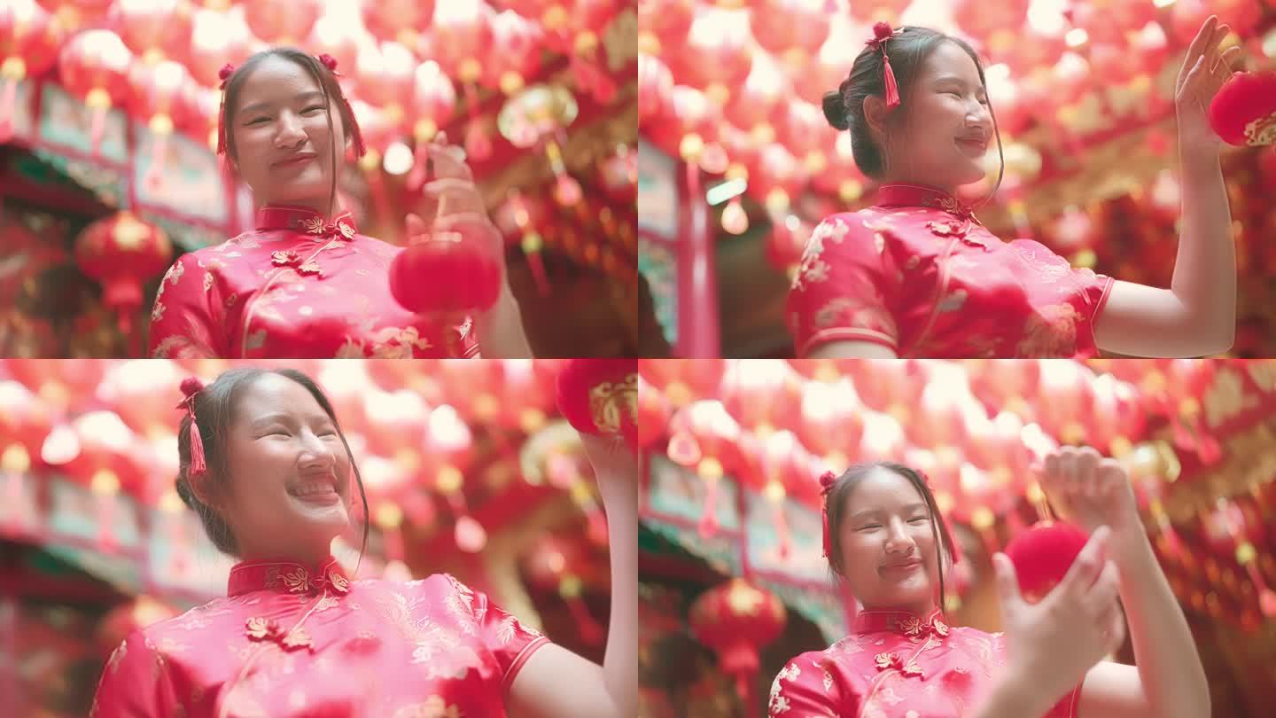 年轻的，红头发的亚洲女孩旗袍正在玩一个深红色的纸灯笼。在中国寺庙里面对镜头咧嘴大笑。