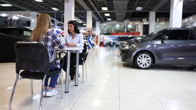 一名拉丁美洲的女销售员在一家汽车经销店与一位不认识的女顾客成交，她非常愉快地握手