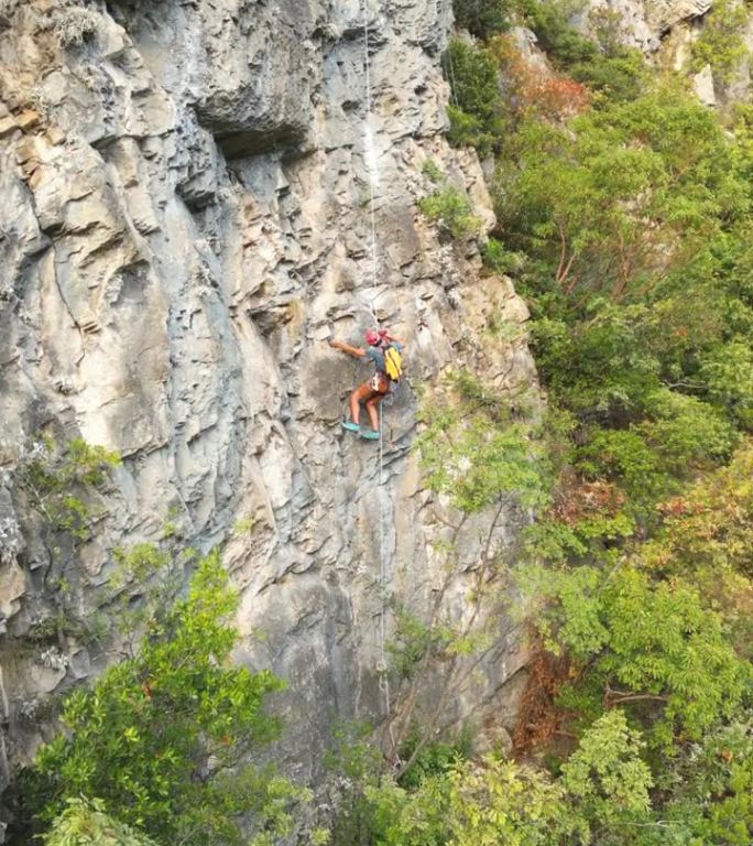 无人机视图创建一个新的攀登路线，使用凿岩机和旋转锤在攀登绳。登山者戴着红色的头盔。