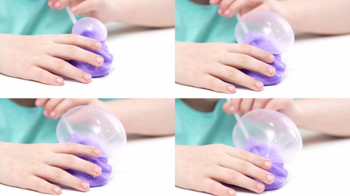 一个孩子玩着一个由亮紫色黏液制成的玩具，用管子吹泡泡，一个时髦的液体玩具粘在他的手上和手指上
