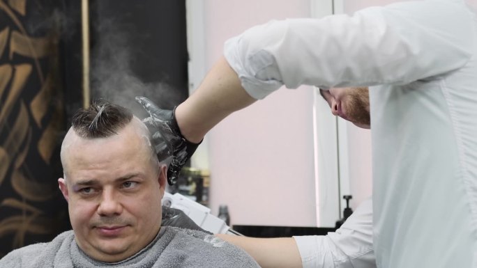 一名理发师在理发店的“热蒸汽剃须”中用直刀给顾客剃头。