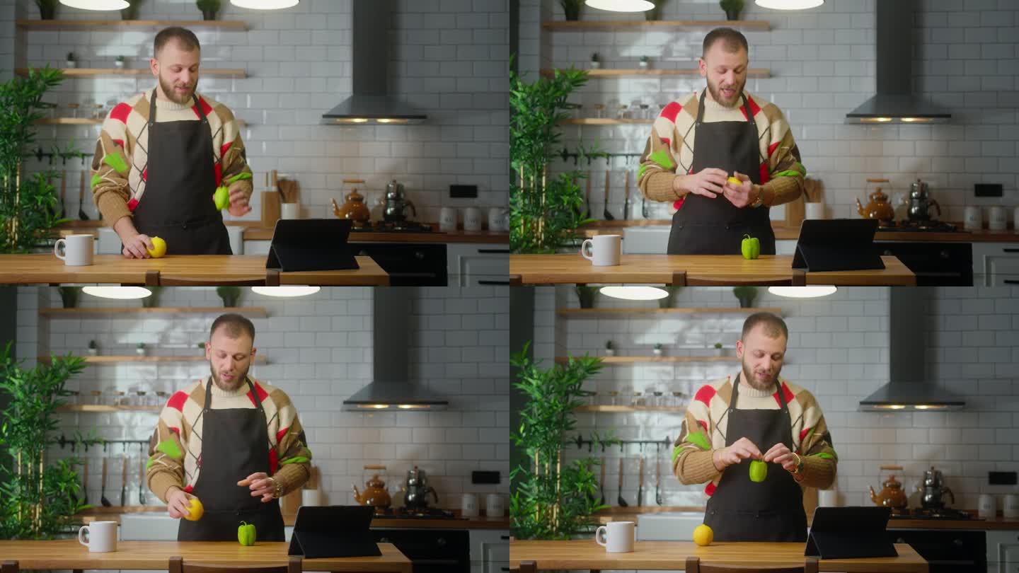 Vlogger男厨师穿着围裙对着平板电脑讲话，在家里的现代厨房里录制关于素食或沙拉的烹饪视频。在线广