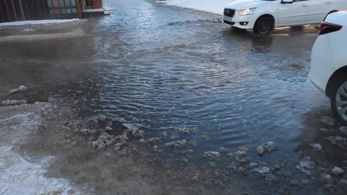 城市街道上的公用设施事故。由于排水系统中断，汽车在冬天被水淹没的道路上行驶。自然灾害使水管爆裂