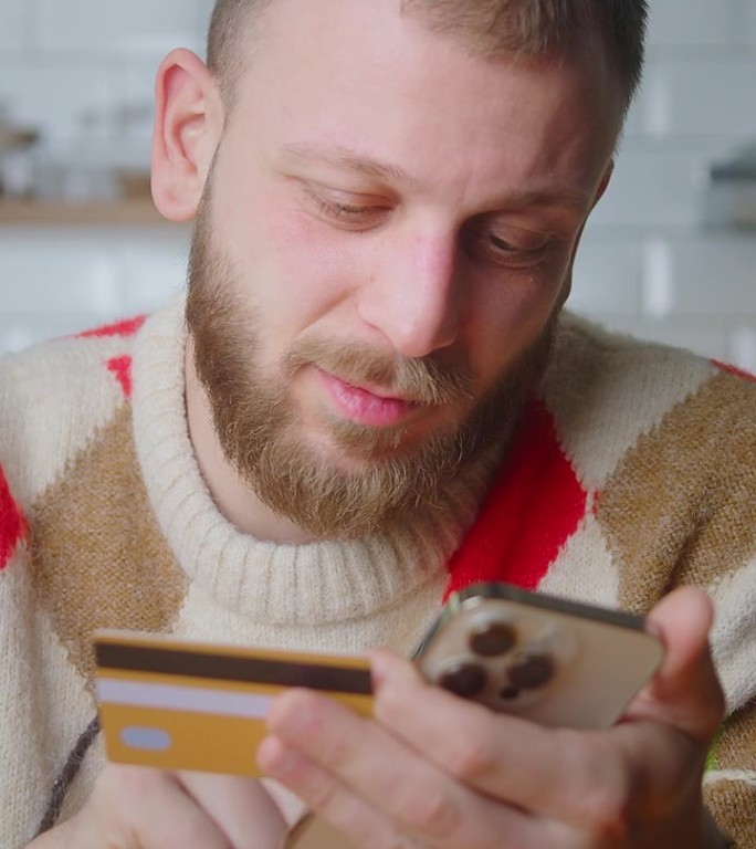 垂直视频。微笑的男子拿着信用卡和智能手机，在网上购物时输入信用卡号码。人们使用即时便捷的移动支付，在