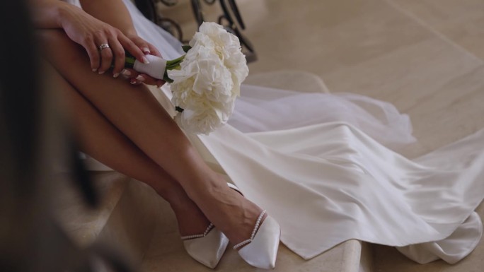 新娘身着礼服，手捧花束的双腿。新娘正坐在台阶上。
