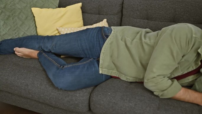 在舒适的客厅里，一个戴着眼镜的英俊男子睡在灰色的沙发上，沙发上有五颜六色的靠垫。