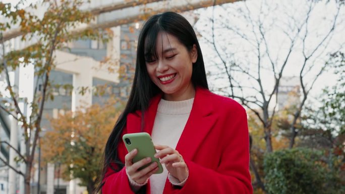 一名日本女子在城市里用手机阅读有趣的通知、社交媒体帖子和下载数字应用程序。快乐的女士在东京的城市公园