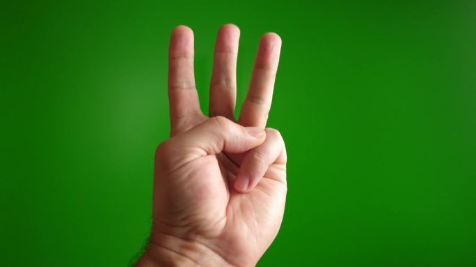 人类的手在绿色背景上显示三个手指向上的手势。