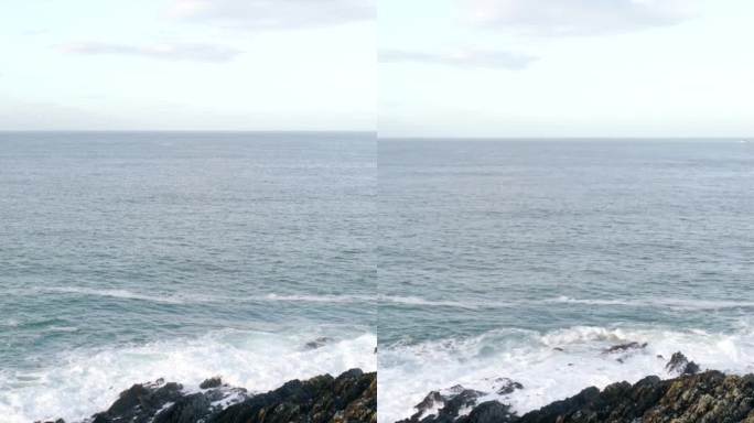 岩石嶙峋的海岸线，锯齿状的岩石在无情的海浪中屹立不倒。深蓝色的大海和白色的浪花。垂直视频，平移。