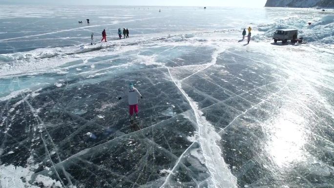 航拍的女孩在贝加尔湖冰封的蓝色透明冰面上滑冰，冰面上有裂缝。自然地标。冬天的风景。热门旅游目的地。