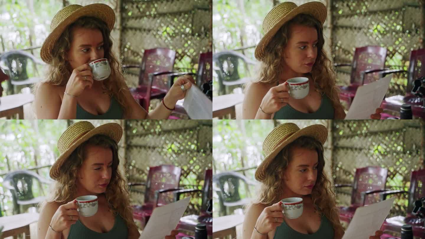 戴草帽的妇女啜着肉桂茶，在雨林小屋阅读游览传单。游客享受芳香的饮料，探索热带环境的活动。在旅途中与自