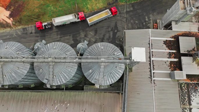 无人机拍摄满载谷物的拖车沿着农场的筒仓行驶