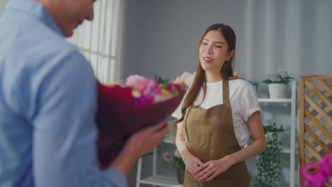 亚洲年轻的花店女孩在店里向顾客兜售漂亮的花束。有魅力的女小企业主在花店给男买家送鲜花礼物时感到快乐和