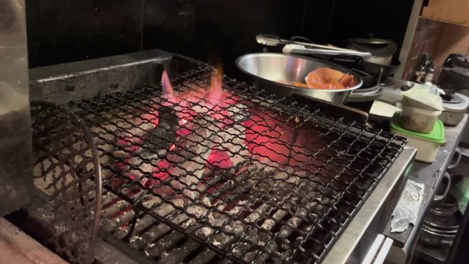 在日本一家餐厅的厨房里，人们正在燃烧网架的炭火。
