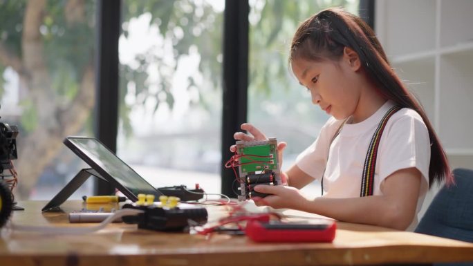 年轻的亚洲女孩在她的平板电脑的在线教程的帮助下学习组装汽车机器人