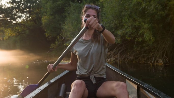 女人在平静的薄雾河上的独木舟上欣赏日落